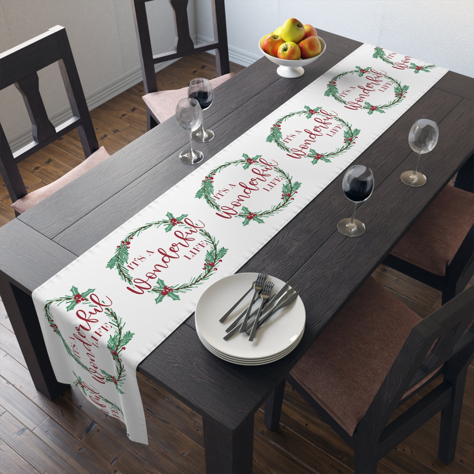 This white Christmas table runner features red lettering that says It's A Wonderful Life inside a holly berry wreath.