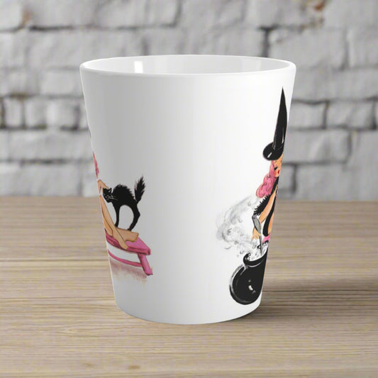 This ceramic glossy latte mug features a retro MidCentury witch with pink hair sitting on a pink bench. She is petting her black cat and stirring her cauldron.