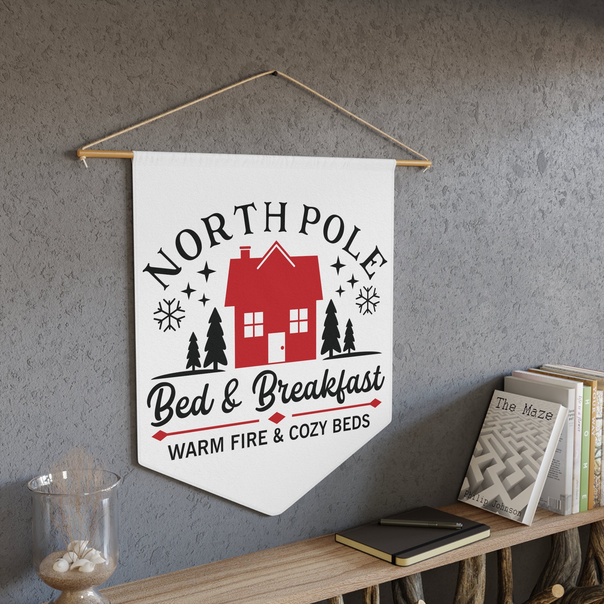 This white Christmas wall hanging pennant banner flag says North Pole Bed and Breakfast Warm Fire and Cozy Beds. It features a red house with trees and stars.