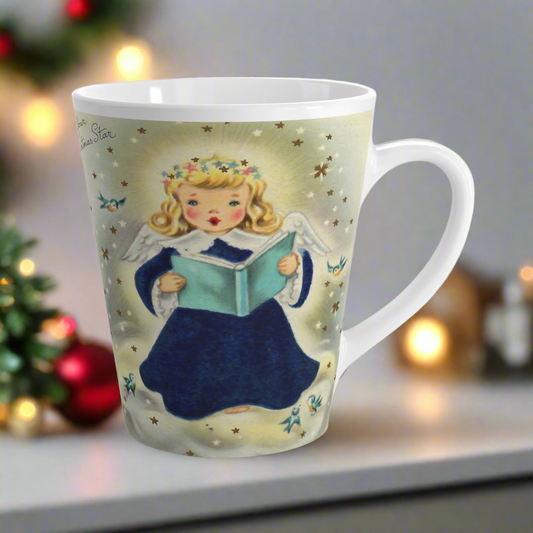 This glossy ceramic Christmas latte mug features a vintage illustration of a blond angel holding a blue book and is singing. There are bluebirds and stars surrounding her. She is wearing a star crown.