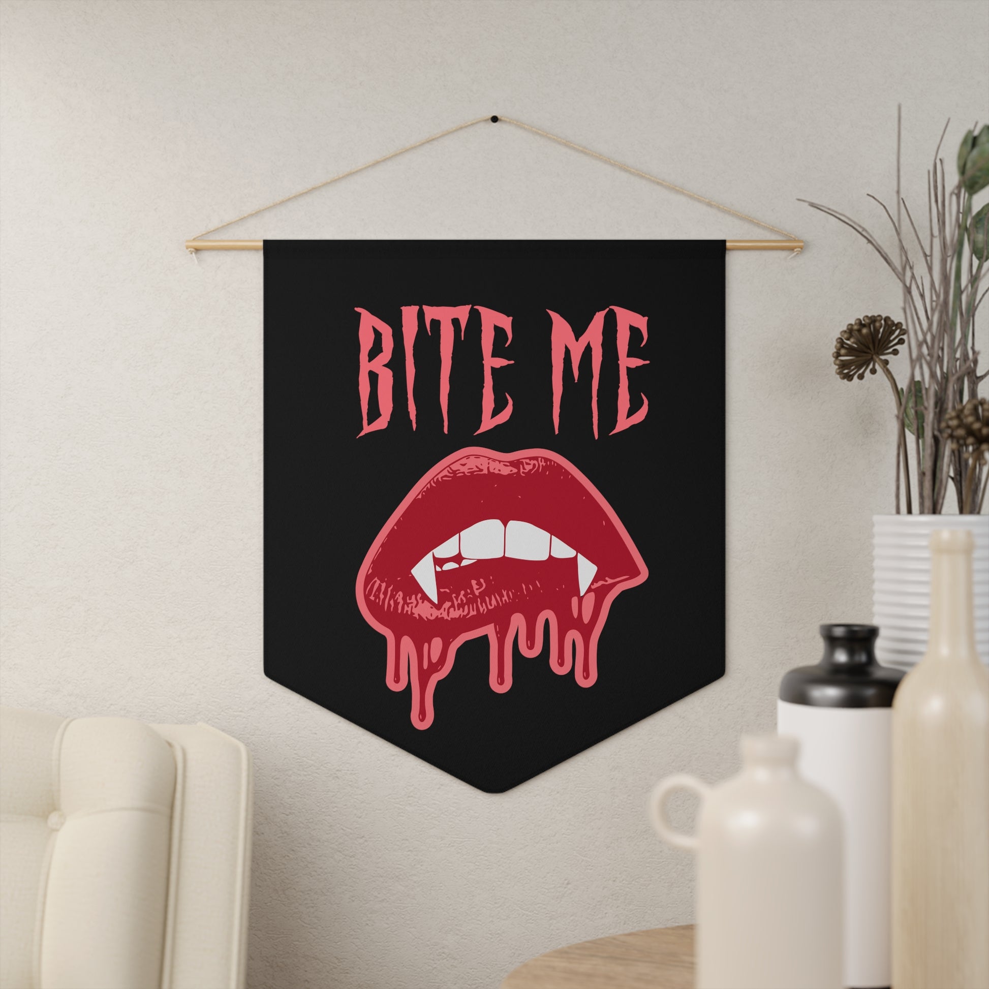 This pennant banner wall hanging features pink gothic lettering that says Bite Me with vampire lips and fangs dripping with blood beneath. 