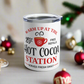 This white 10 ounce stainless steel tumbler mug says Warm Up At The Hot Cocoa Station Served Daily. 25 cent free refills. There is a little red coffee cup with a snowflake on it.