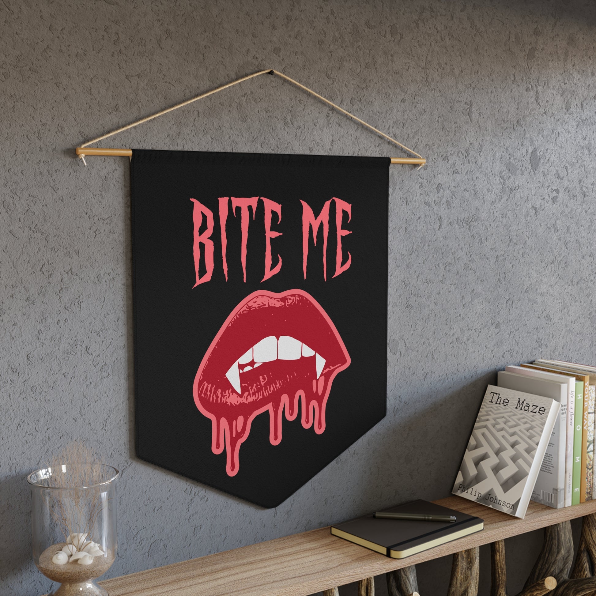 This pennant banner wall hanging features pink gothic lettering that says Bite Me with vampire lips and fangs dripping with blood beneath. 