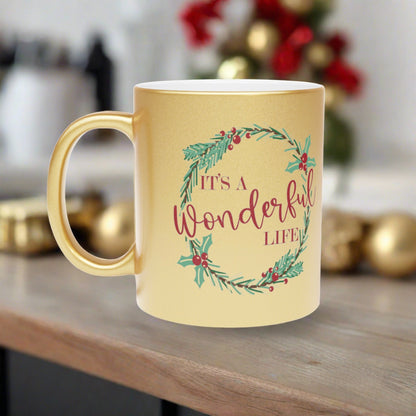 This gold metallic ceramic mug features a holly wreath with red lettering that says It's a Wonderful Life.