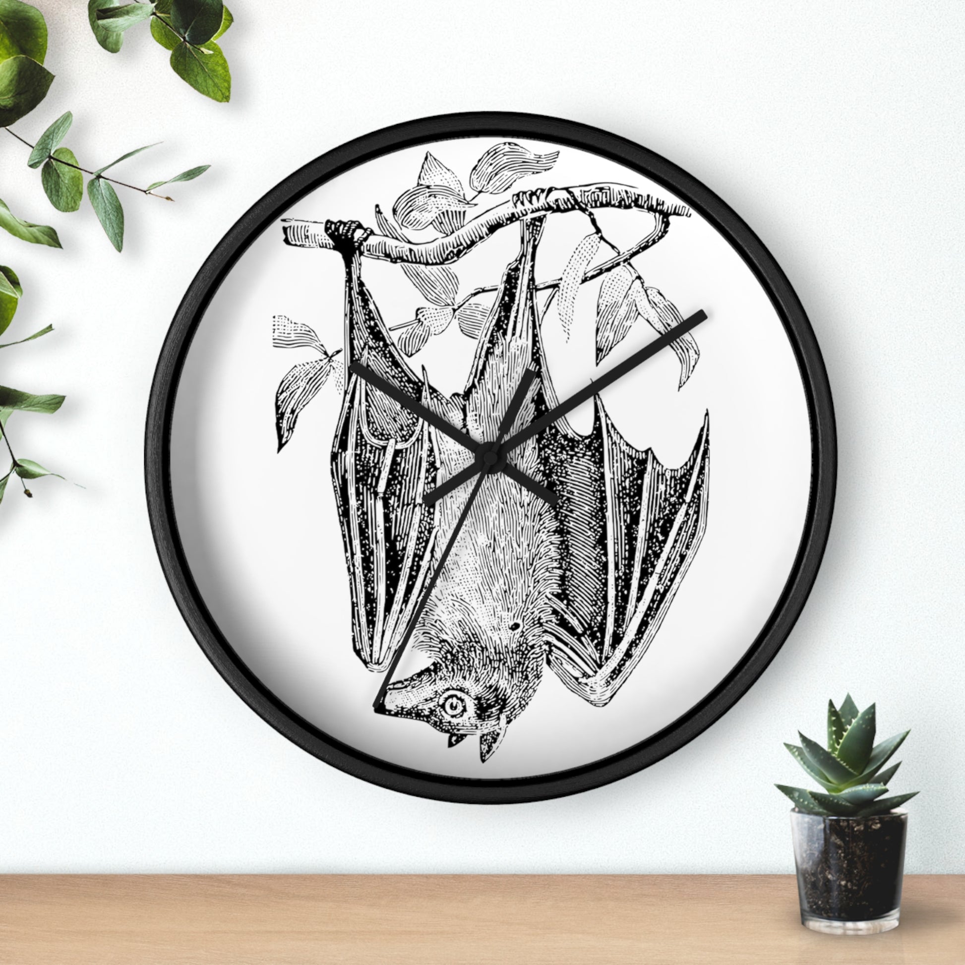 This black wall clock features a vintage illustration of a bat hanging upside down from a branch. The frame and hands of the clock are black.