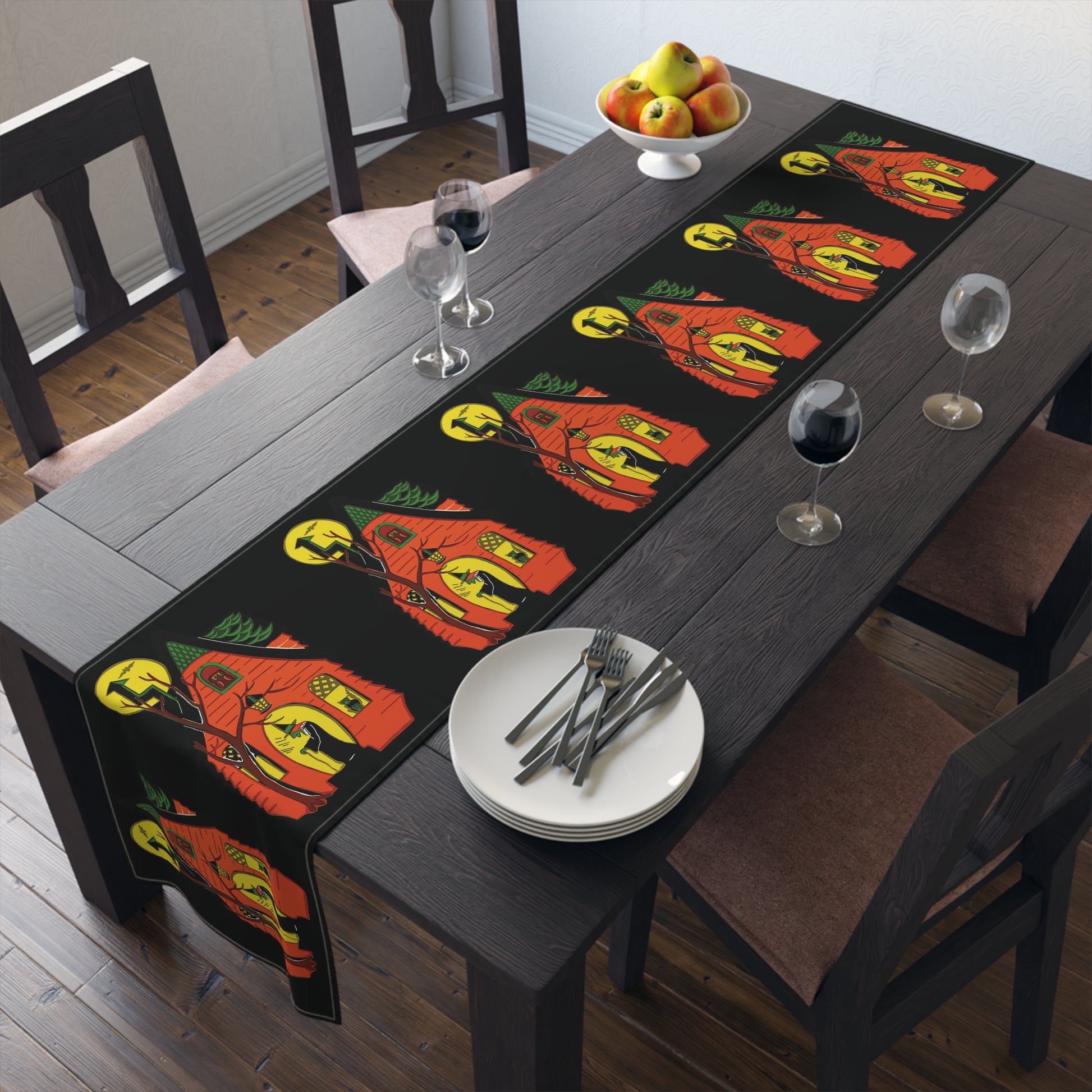 This black table runner features a retro Halloween print of a green witch in front of her orange house with her black cat in the window and a yellow moon in the sky.