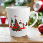 This ceramic glossy latte coffee mug features a midcentury retro illustration of red reindeer and green christmas trees with red ornaments.