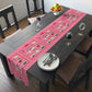 The pink Christmas table runner features the AriesCat Christmas Cocktails design. It features different midcentury style cocktails artwork with a red square present bow around them. 