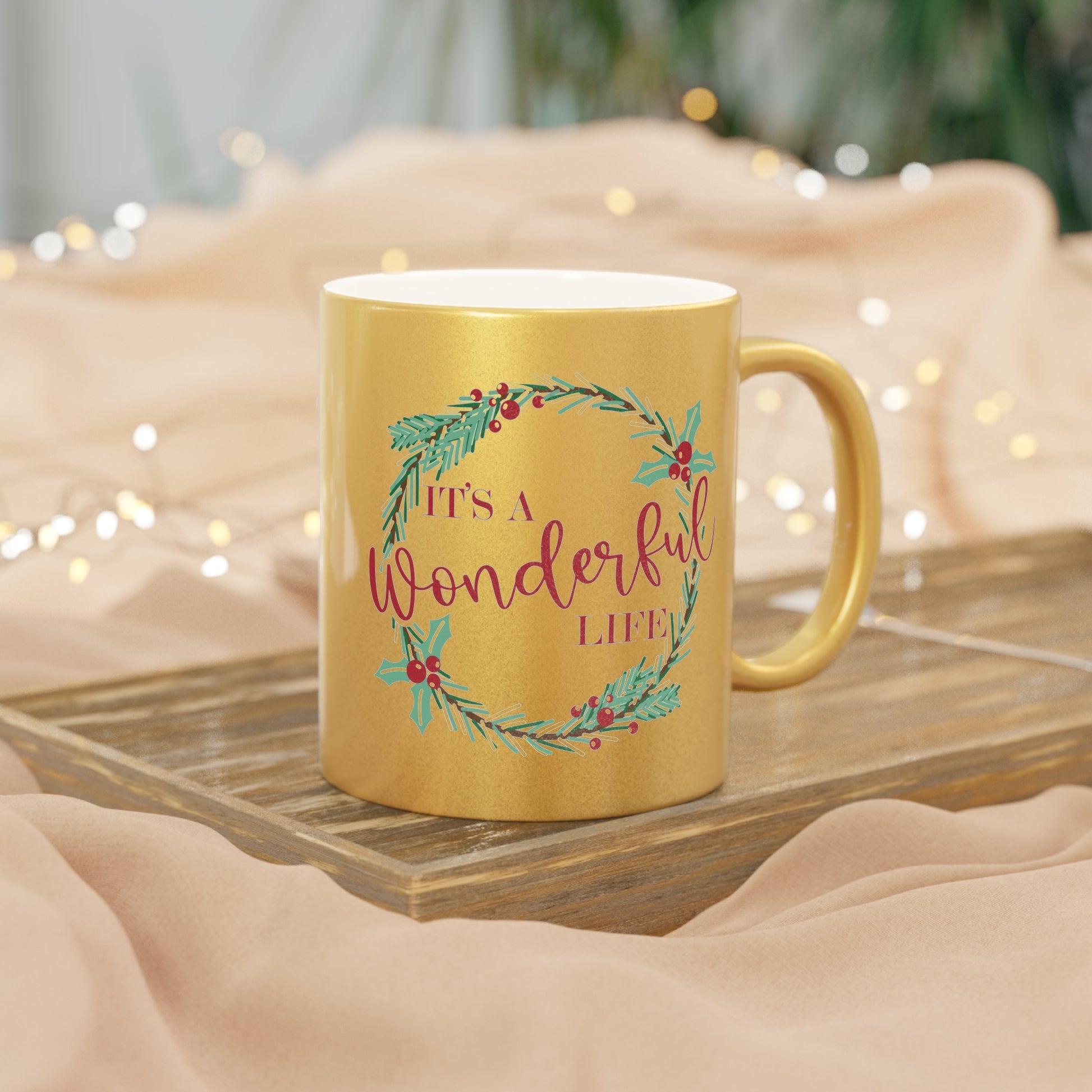 This gold metallic ceramic mug features a holly wreath with red lettering that says It's a Wonderful Life.