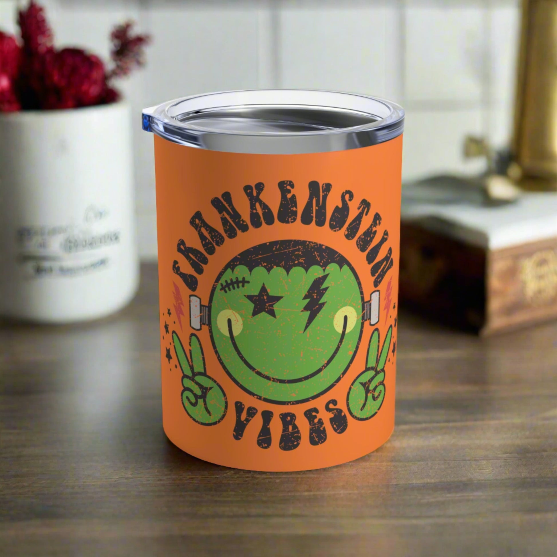 This 10 ounce orange stainless steel travel tumbler says Frankenstein Vibes and features a cute green monster smiley face with stars and lightning bolts.