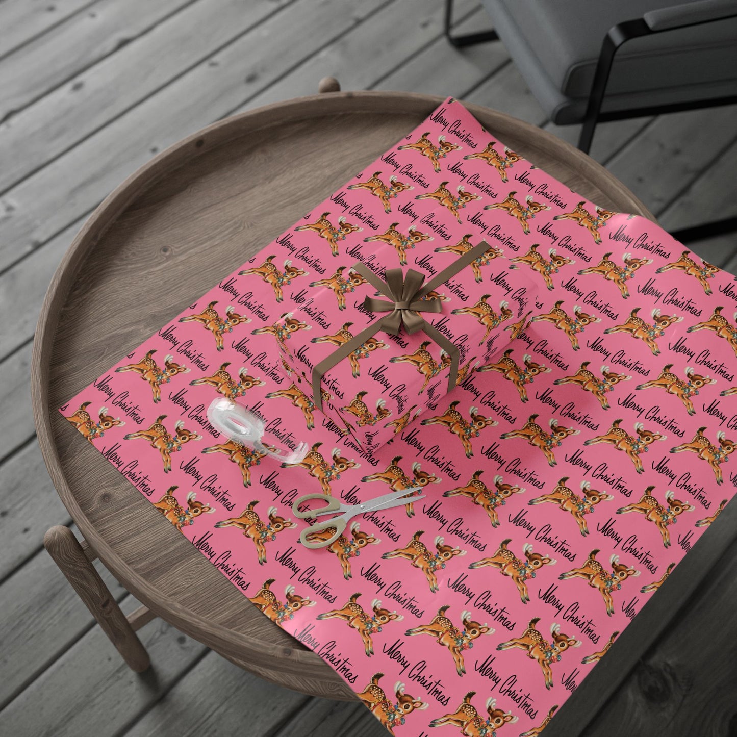 This pink gift wrap features a midcentury illustration of a leaping reindeer adorned with an ornament wreath around her neck. There is black lettering that says Merry Christmas.