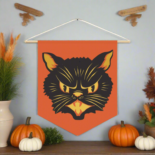 This orange fabric wall hanging pennant banner features a vintage Halloween Illustration of a beautiful black cat with orange and yellow eyes, nose, mouse and ears. The wall hanging comes with a wooden dowel and twine frame.