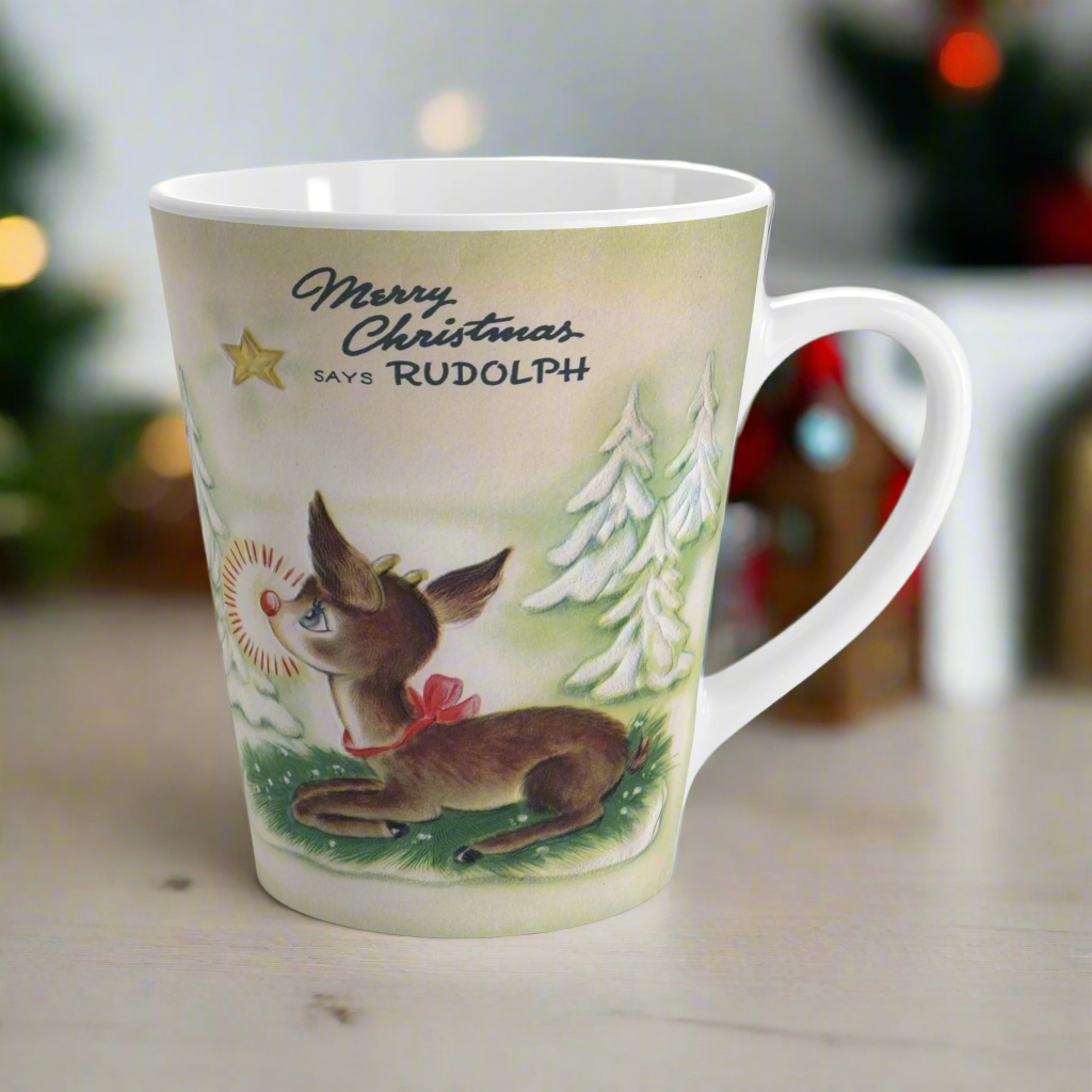 This ceramic latte coffee mug features a midcentury vintage Christmas illustration featuring Rudolph the Red Nosed Reindeer sitting down looking up at a gold star in the sky surrounded by snowy trees. It says: Merry Christmas Says Rudolph.