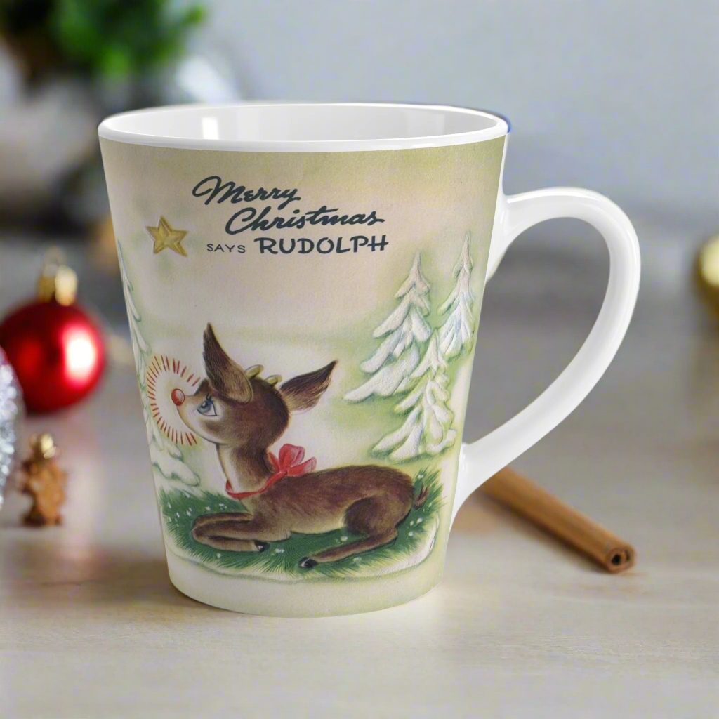 This ceramic latte coffee mug features a midcentury vintage Christmas illustration featuring Rudolph the Red Nosed Reindeer sitting down looking up at a gold star in the sky surrounded by snowy trees. It says: Merry Christmas Says Rudolph.