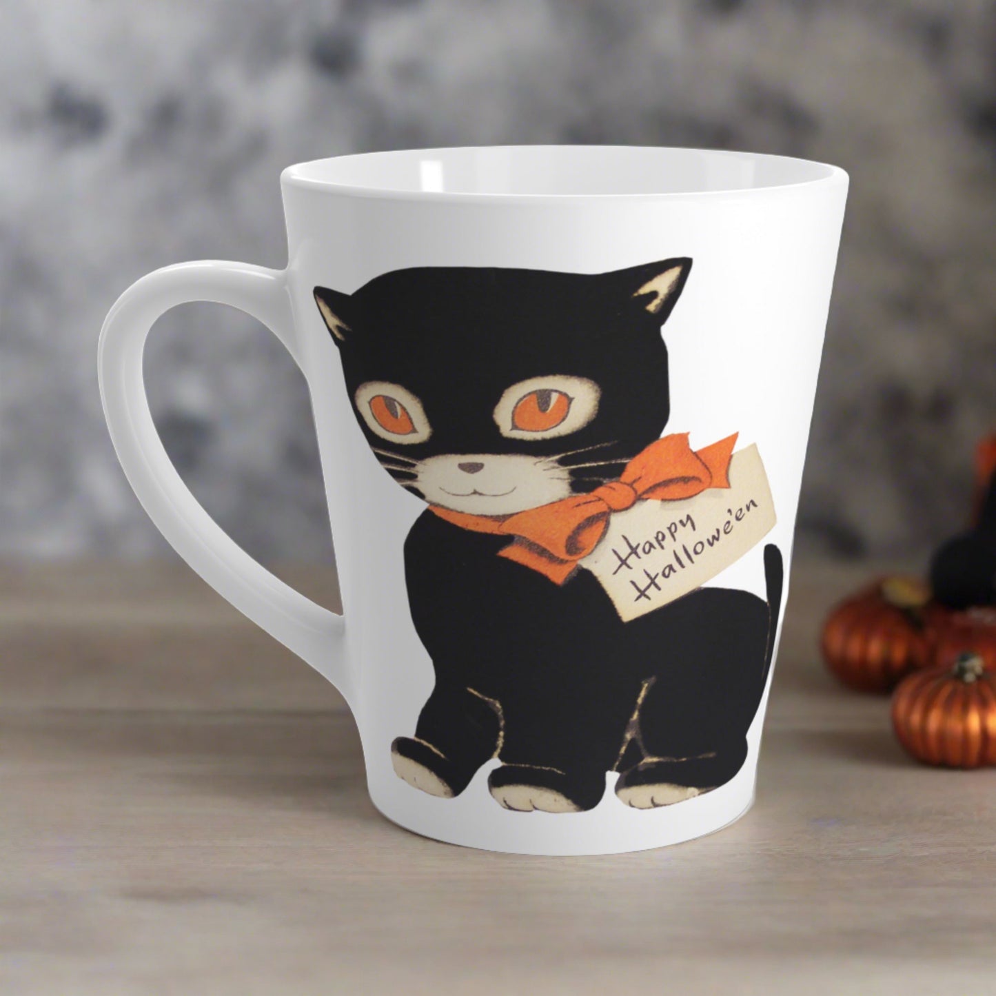 This glossy ceramic latte mug features a retro vintage Halloween illustration of a black cat with orange eyes. She is wearing an orange bow with a tag that says Happy Halloween.