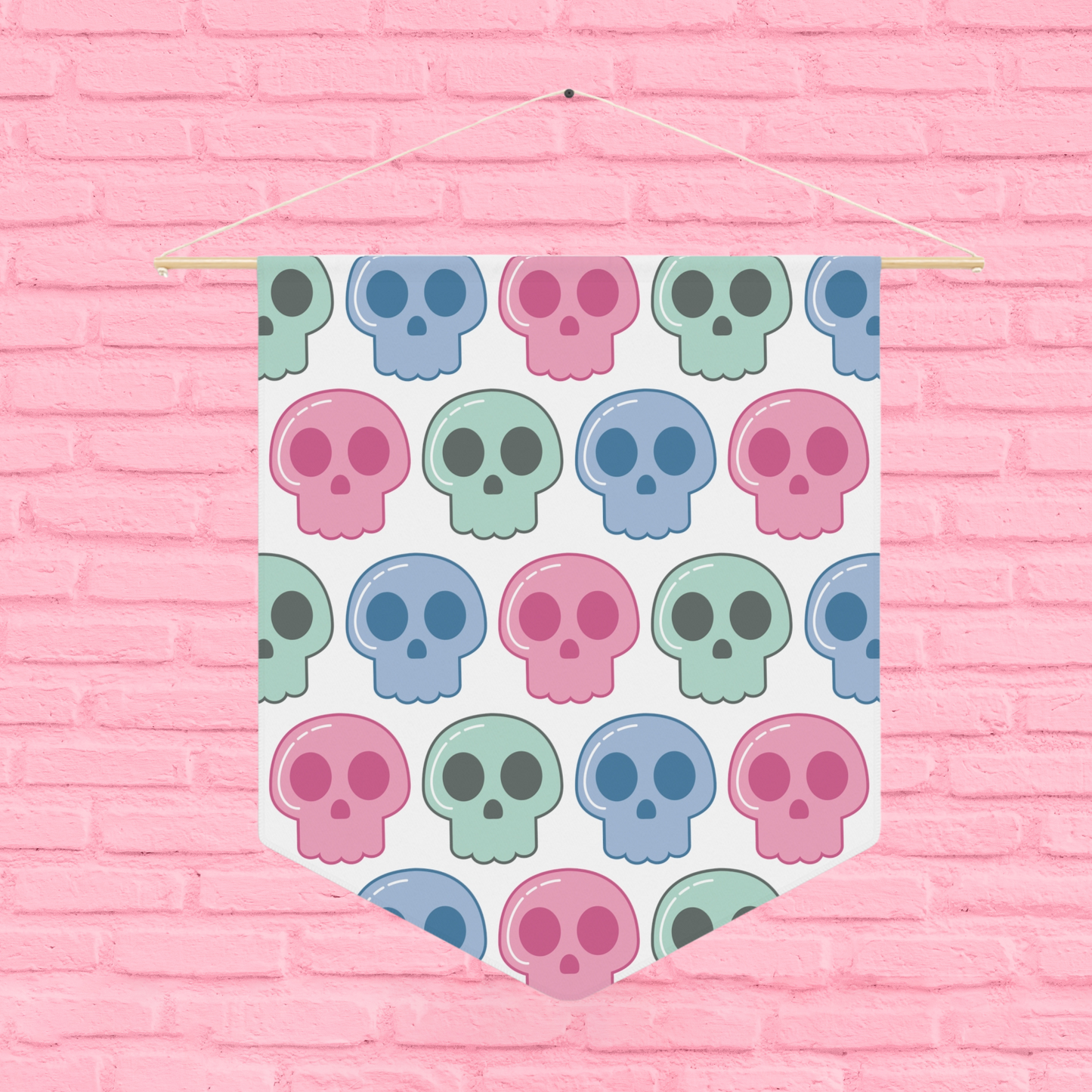 This pennant banner wall hanging features cute pastel goth skulls patterned in pink, green and blue with a white background on fabric canvas. It hands on a wooden dowel.