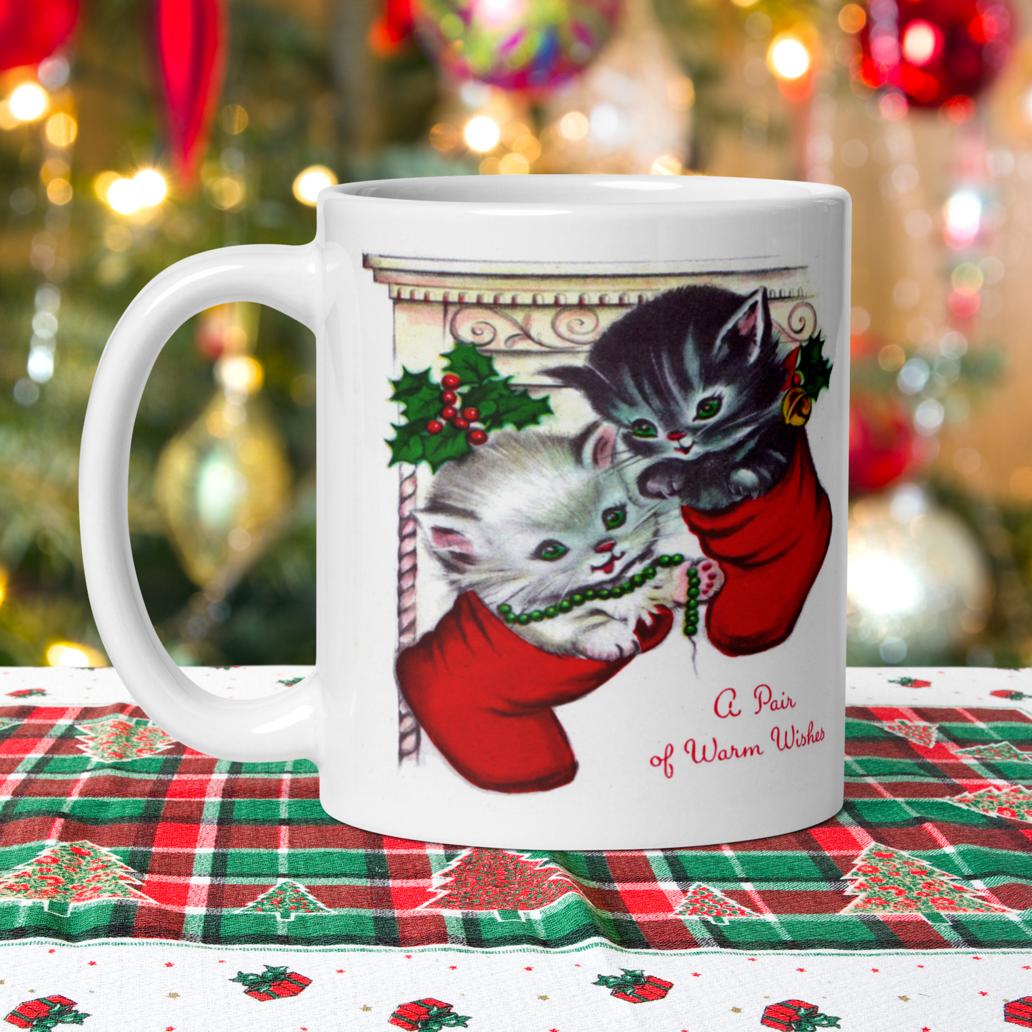 This white ceramic glossy coffee mug features two adorable kittens in red stockings at a Christmas mantle. The print is retro kitsch and says A Pair of Warm Wishes.