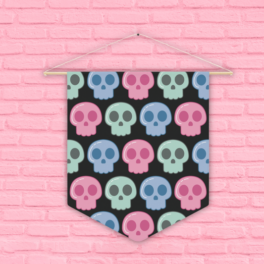 This pennant banner wall hanging features cute pastel goth skulls in pink, green and blue with a black background. The wall hanging hangs on a wooden dowel.