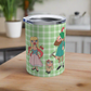 This 10 ounce travel tumbler mug features characters from the Sound of Music Lonely Goatherd song: The Goatherd, the girl in the pale pink coat, and the baby goat. The background is green plaid. The mug comes with a plastic sipping lid.