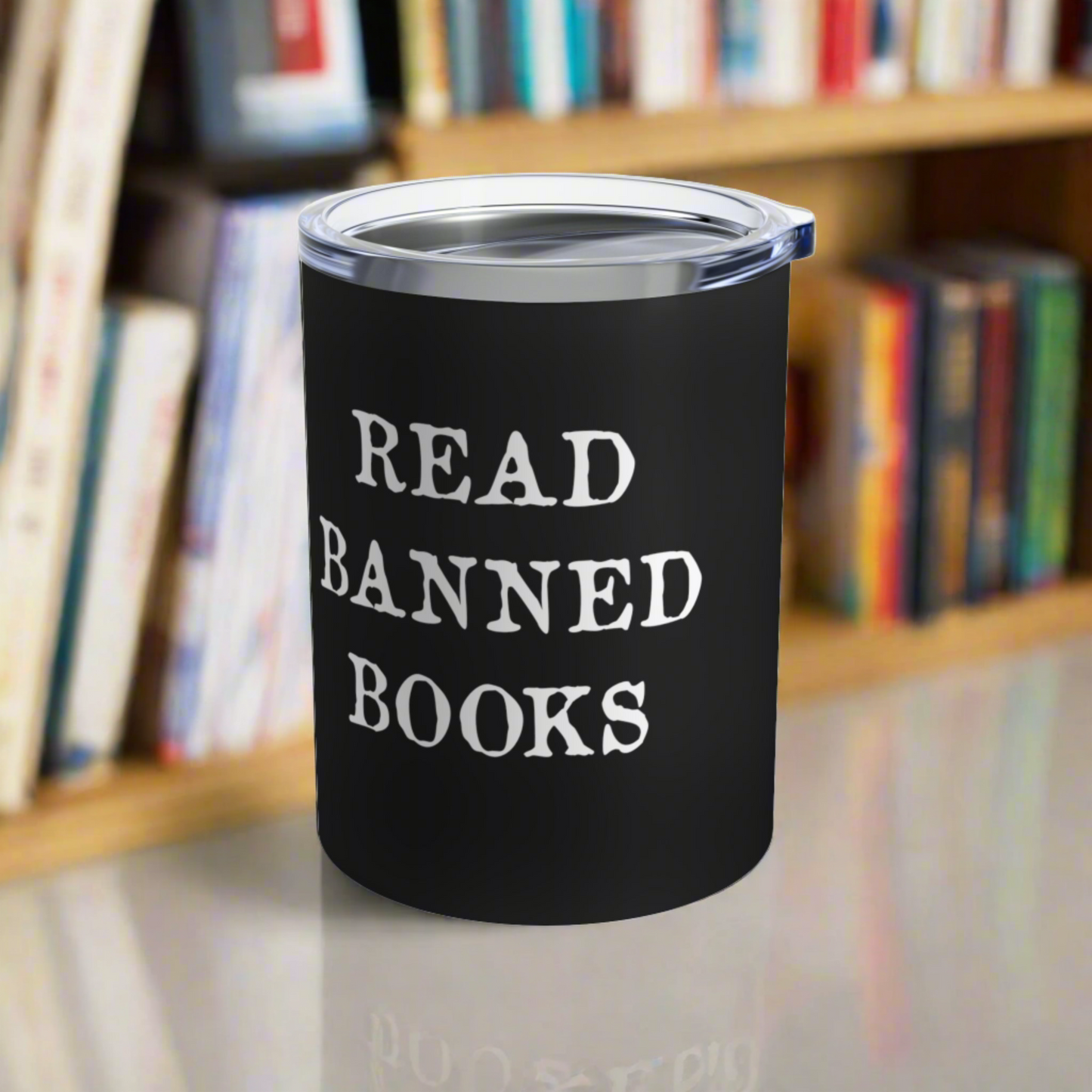 This 10 ounce black stainless steel insulated travel tumbler mug features white letters that say Read Banned Books. The tumbler comes with a plastic sipping lid.