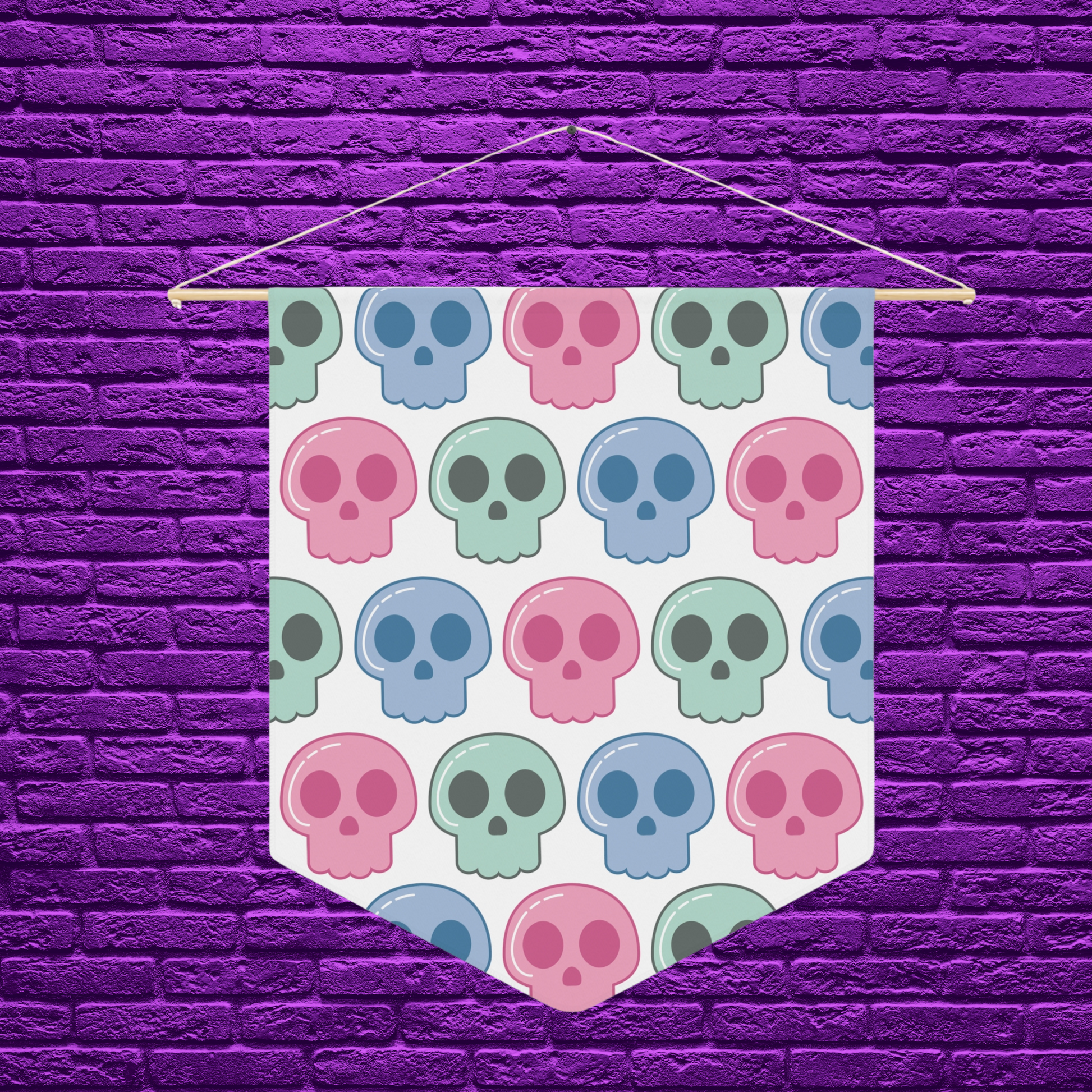 This pennant banner wall hanging features cute pastel goth skulls patterned in pink, green and blue with a white background on fabric canvas. It hands on a wooden dowel.