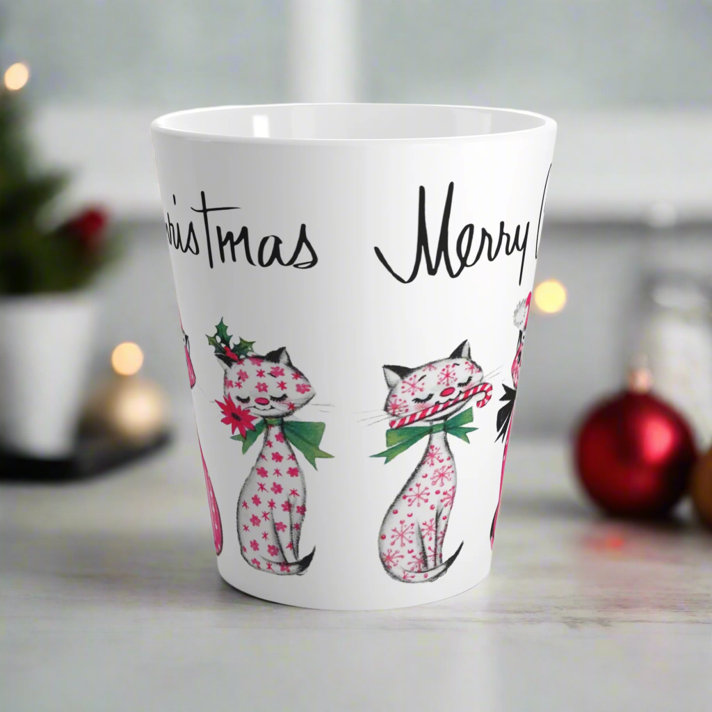 This ceramic latte coffee mug says Merry Christmas in midcentury lettering and features 3 adorable midcentury retro Christmas cats. They are pink with different patterns. They each have a bow around their neck, one is holding a candy cane in their mouth, one is wearing a pink santa hat and one has a flower in her mouth. Nostalgic and adorable. 