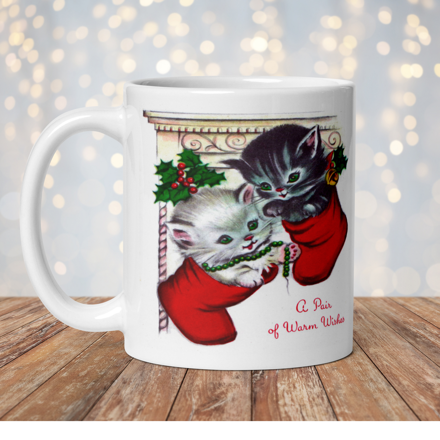 This white ceramic glossy coffee mug features two adorable kittens in red stockings at a Christmas mantle. The print is retro kitsch and says A Pair of Warm Wishes.