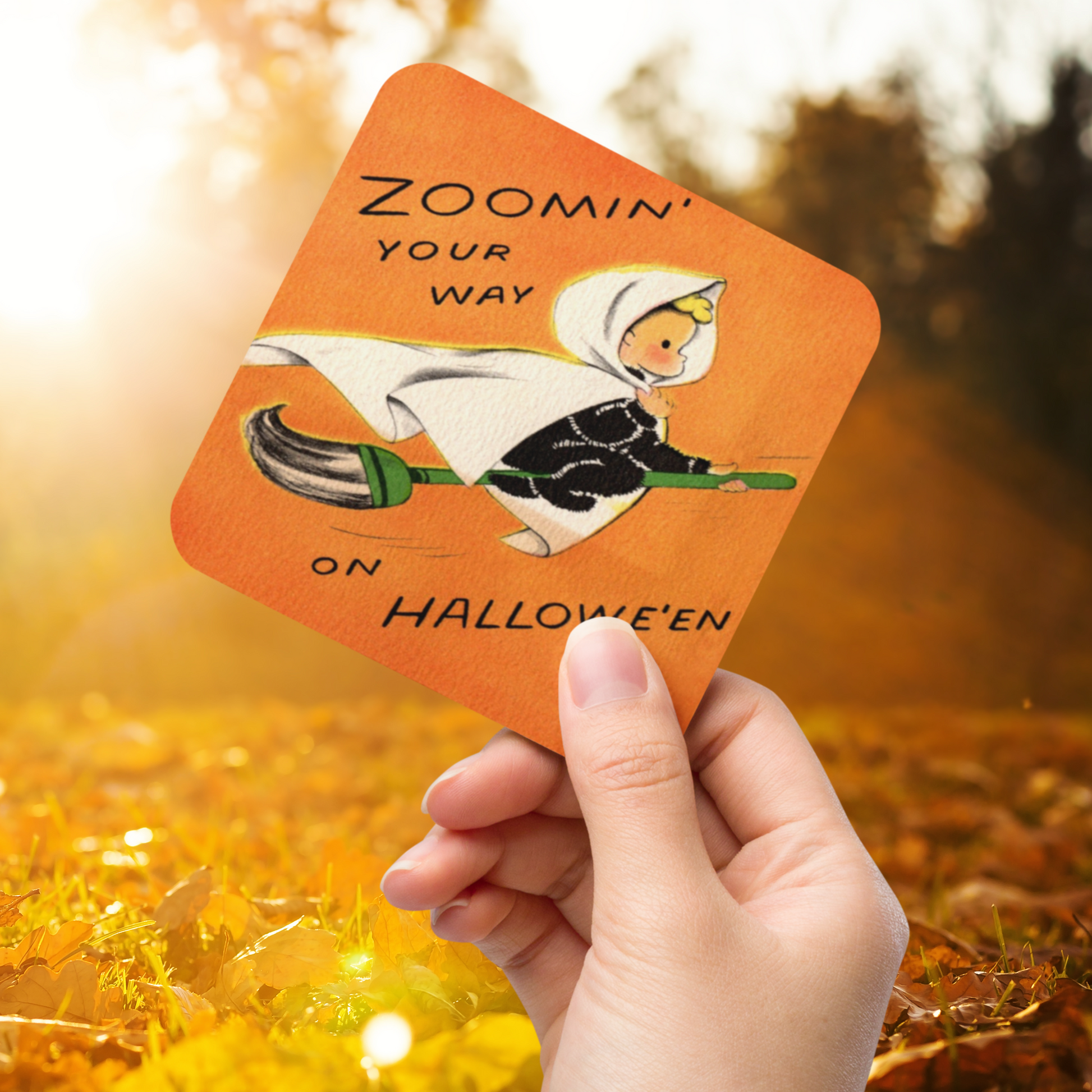 This orange glossy cork back coaster features a retro Halloween illustration that says Zoomin' Your Way On Halloween with an adorable witch flying on a broomstick.