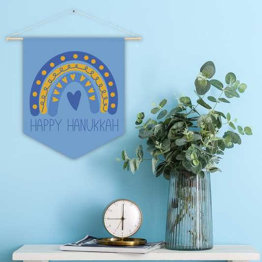 This blue pennant banner wall hanging features a blue boho rainbow with a heart and says Happy Hanukkah.