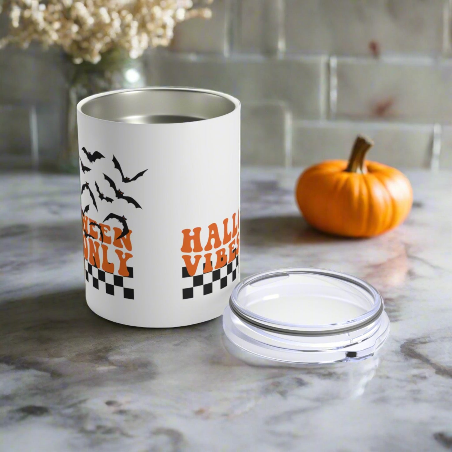 This 10 ounce stainless steel travel tumbler mug features orange retro lettering that says Halloween Vibes Only with black and white checkered print with flying bats. 