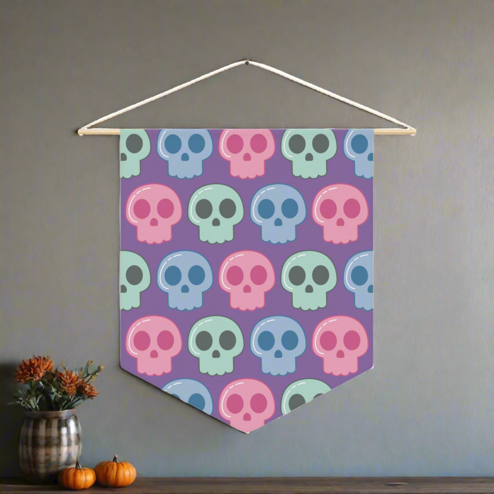 This fabric wall hanging features pastel skulls in pink, green and blue with a purple background. They are staggered in a pattern.