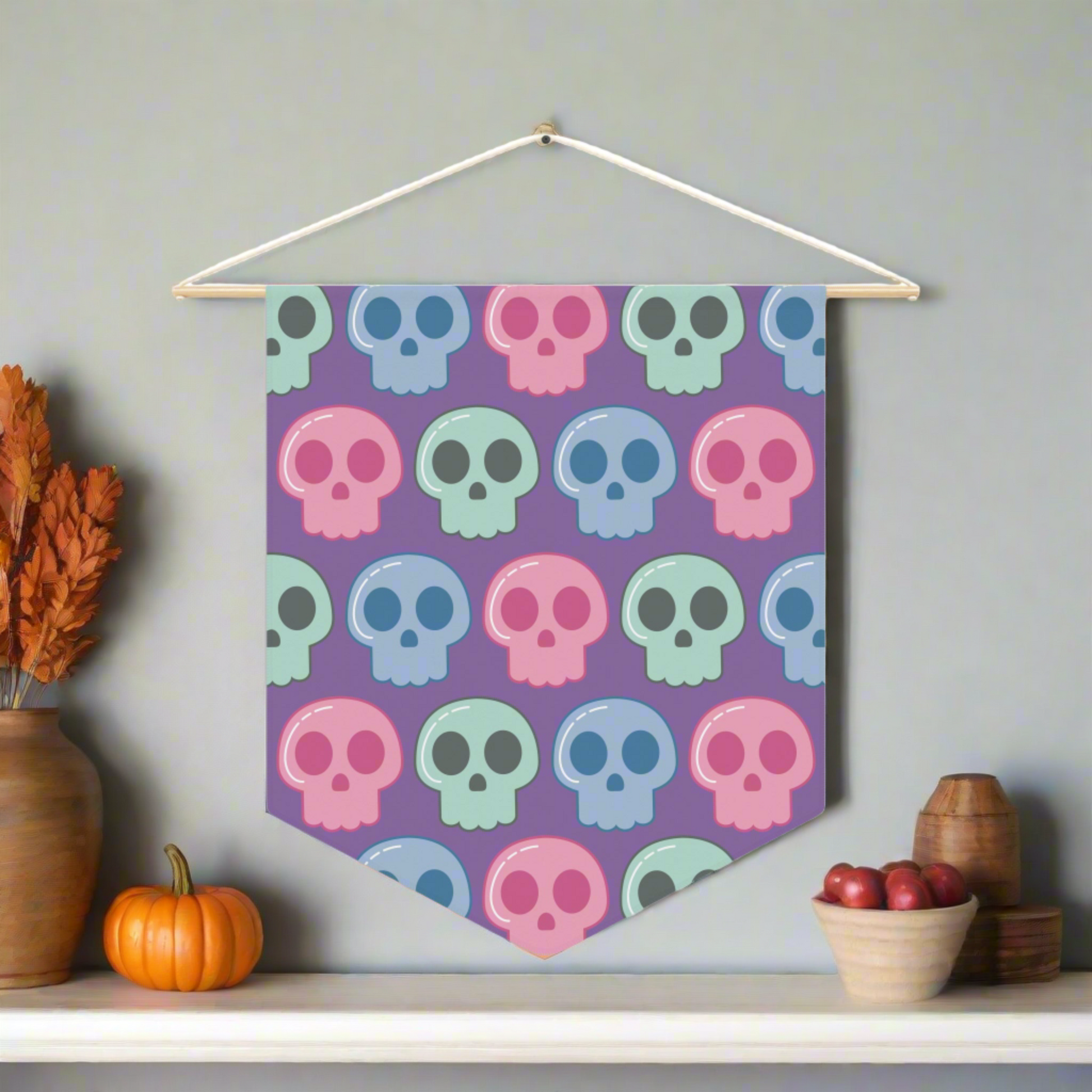 This fabric wall hanging features pastel skulls in pink, green and blue with a purple background. They are staggered in a pattern.