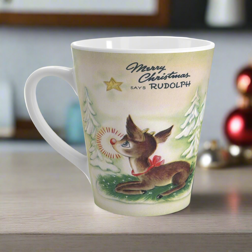 This ceramic latte coffee mug features a midcentury vintage Christmas illustration featuring Rudolph the Red Nosed Reindeer sitting down looking up at a gold star in the sky surrounded by snowy trees. It says: Merry Christmas Says Rudolph.