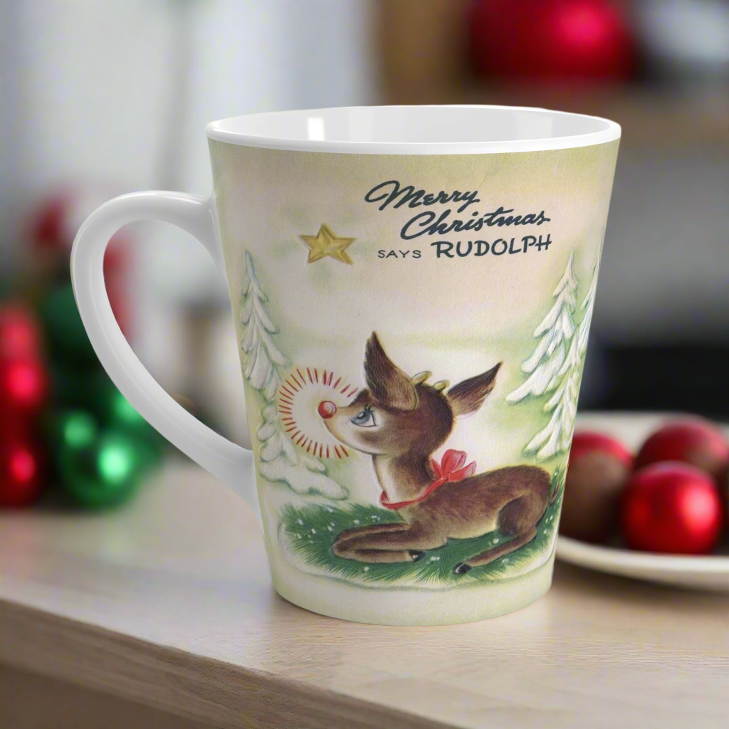 This ceramic latte coffee mug features a midcentury vintage Christmas illustration featuring Rudolph the Red Nosed Reindeer sitting down looking up at a gold star in the sky surrounded by snowy trees. It says: Merry Christmas Says Rudolph.