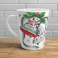 This ceramic glossy latte coffee cup features a vintage Christmas illustration of two holiday bells with ribbon, pine and berries. The design on the bells is reminiscent of European Scandinavian Christmas decorations.