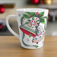 This ceramic glossy latte coffee cup features a vintage Christmas illustration of two holiday bells with ribbon, pine and berries. The design on the bells is reminiscent of European Scandinavian Christmas decorations.