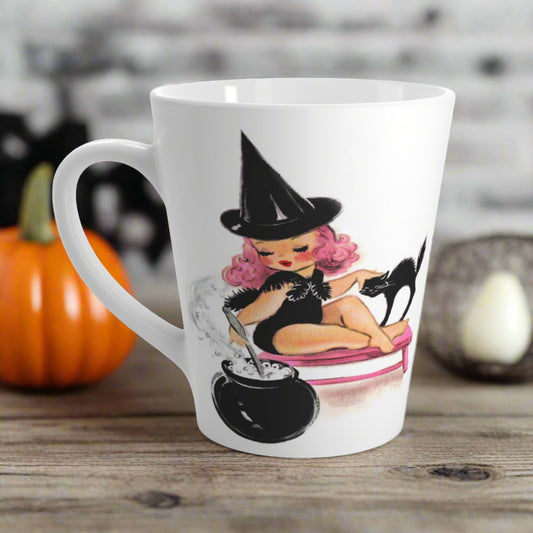 This ceramic glossy latte mug features a retro MidCentury witch with pink hair sitting on a pink bench. She is petting her black cat and stirring her cauldron.