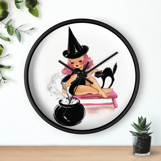 This silent wall clock features a midcentury retro Halloween print of a witch with pink hair petting her black cat and stirring her cauldron. The wooden frame and hands of the clock are black.