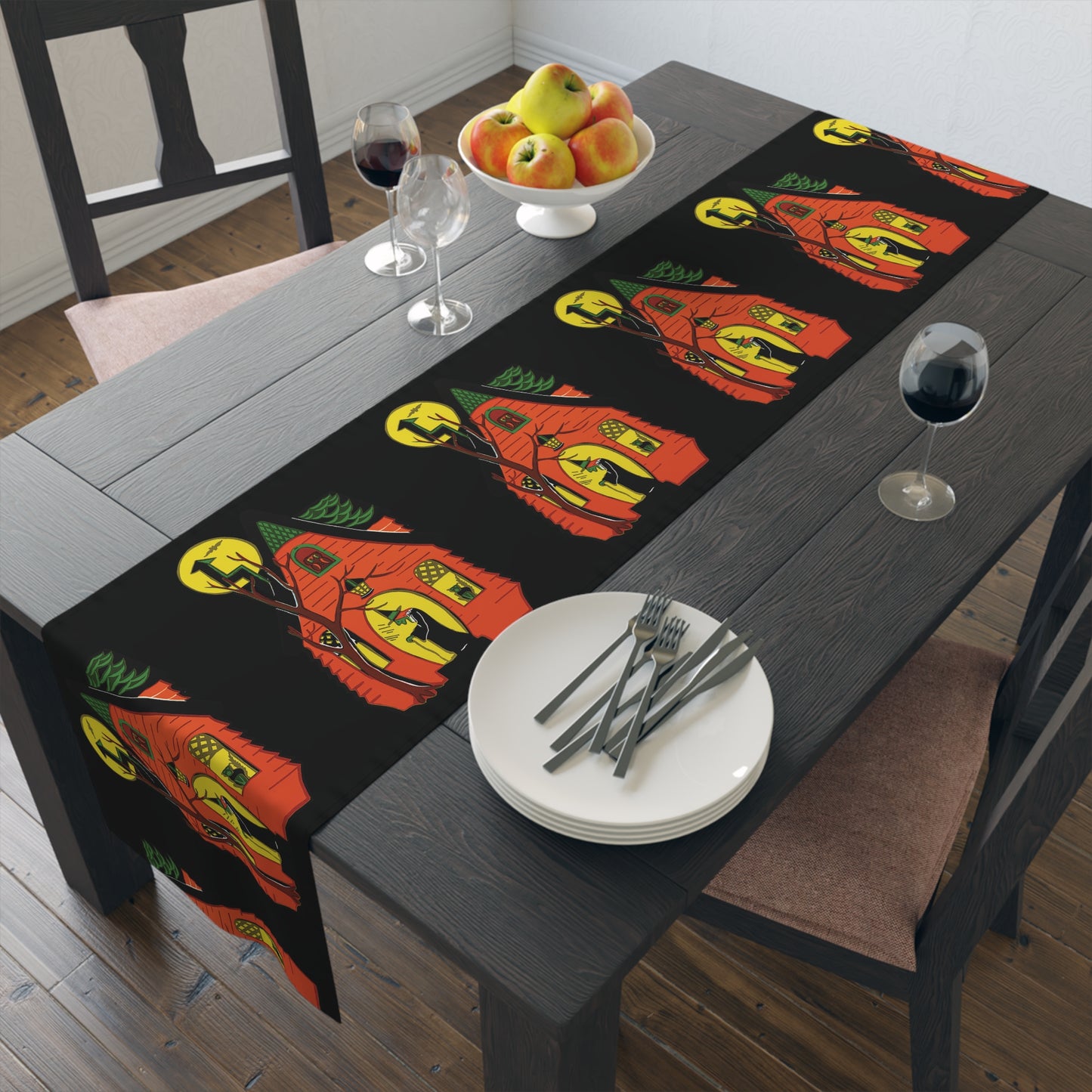 This black table runner features a retro Halloween print of a green witch in front of her orange house with her black cat in the window and a yellow moon in the sky.