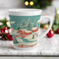 This ceramic glossy latte coffee mug features a vintage winter Christmas illustration of a snowy winter town. There are red houses, a bridge, trees, and two children building a snowman.