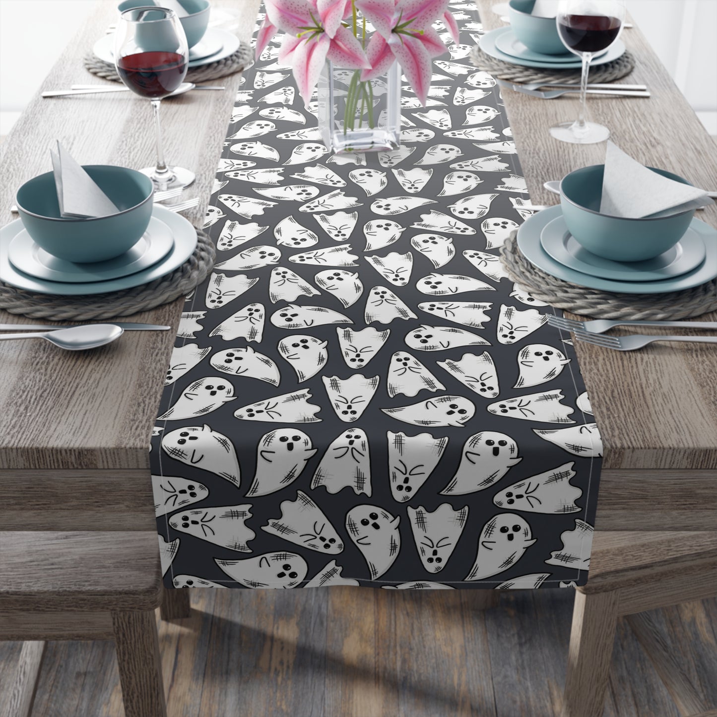 This Halloween table runner features adorable hand drawn ghosts patterned across the cloth with a dark grey background.