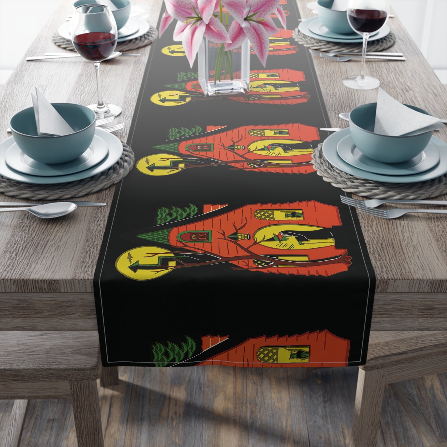 This black table runner features a retro Halloween print of a green witch in front of her orange house with her black cat in the window and a yellow moon in the sky.