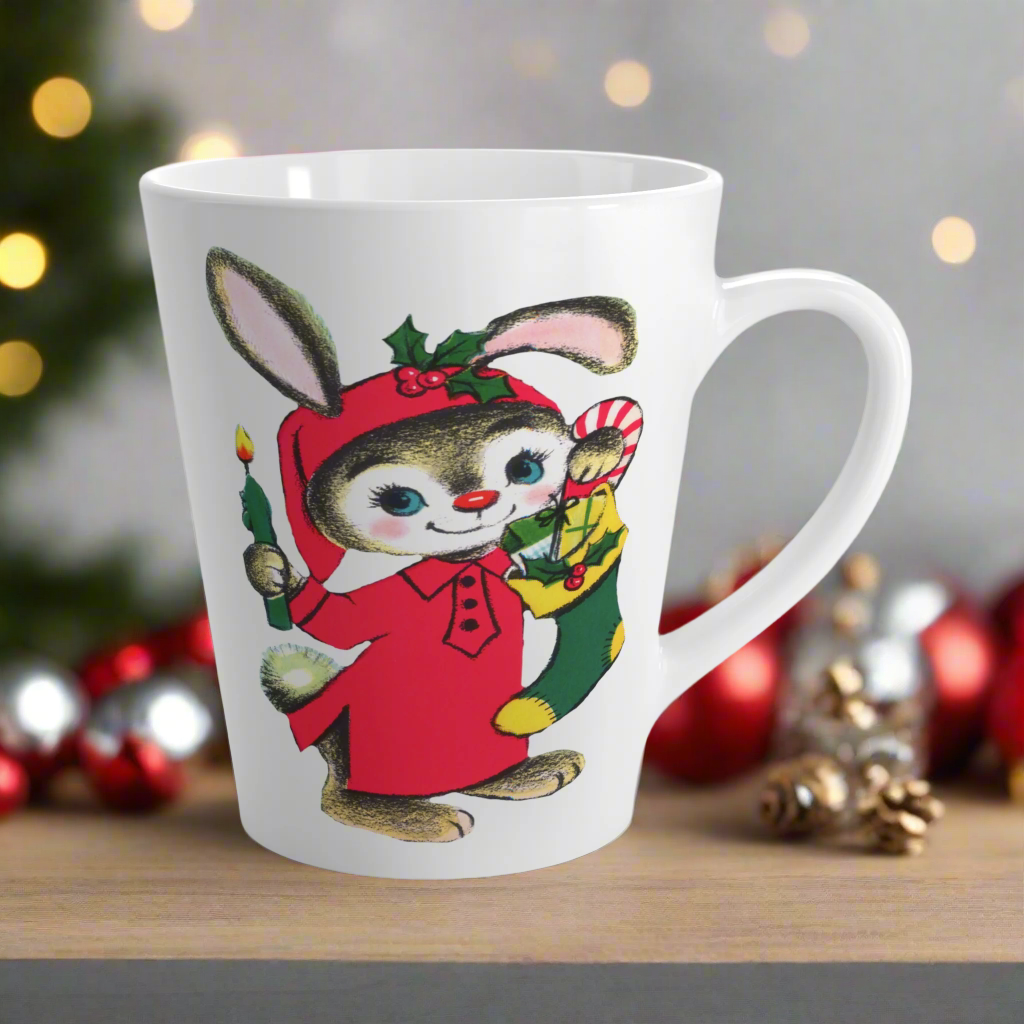 This ceramic glossy latte coffee mug features a midcentury Christmas illustration of an adorable bunny. The bunny is wearing a red sleeping cap and nightgown. He is holding a candle in one hand and a green and yellow christmas stocking with presents.