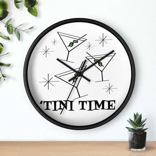 This wall clock features an atomic era design of martini glasses with green olives on toothpicks surrounded by stars with the lettering Tini Time at the bottom. It has a white background. The clock has black hands and a black wooden frame.