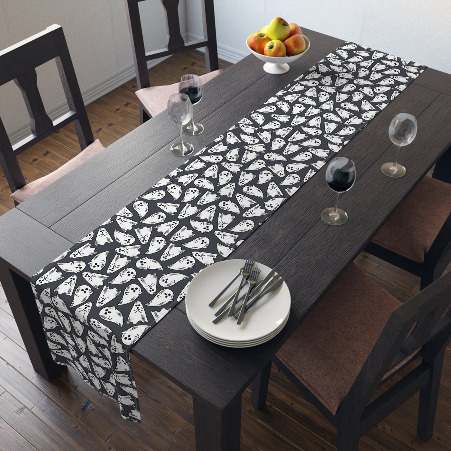 This Halloween table runner features adorable hand drawn ghosts patterned across the cloth with a dark grey background.