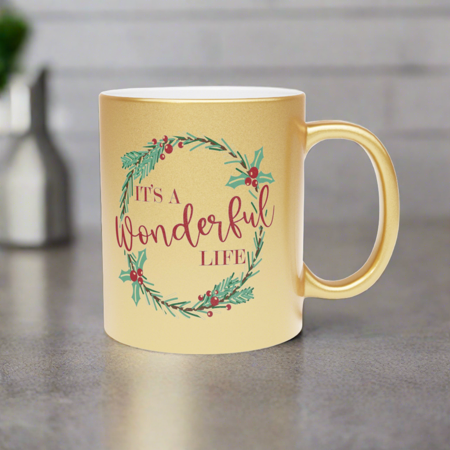 This gold metallic ceramic mug features a holly wreath with red lettering that says It's a Wonderful Life.