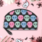 Cute cosmetic makeup travel bag featuring adorable pastel skulls with a black background. The bag has a zipper and a side wristlet.