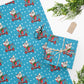 This Christmas gift wrap features a midcentury retro illustration of a cute mouse on a scooter wearing a Santa hat. The background is blue with white stars.