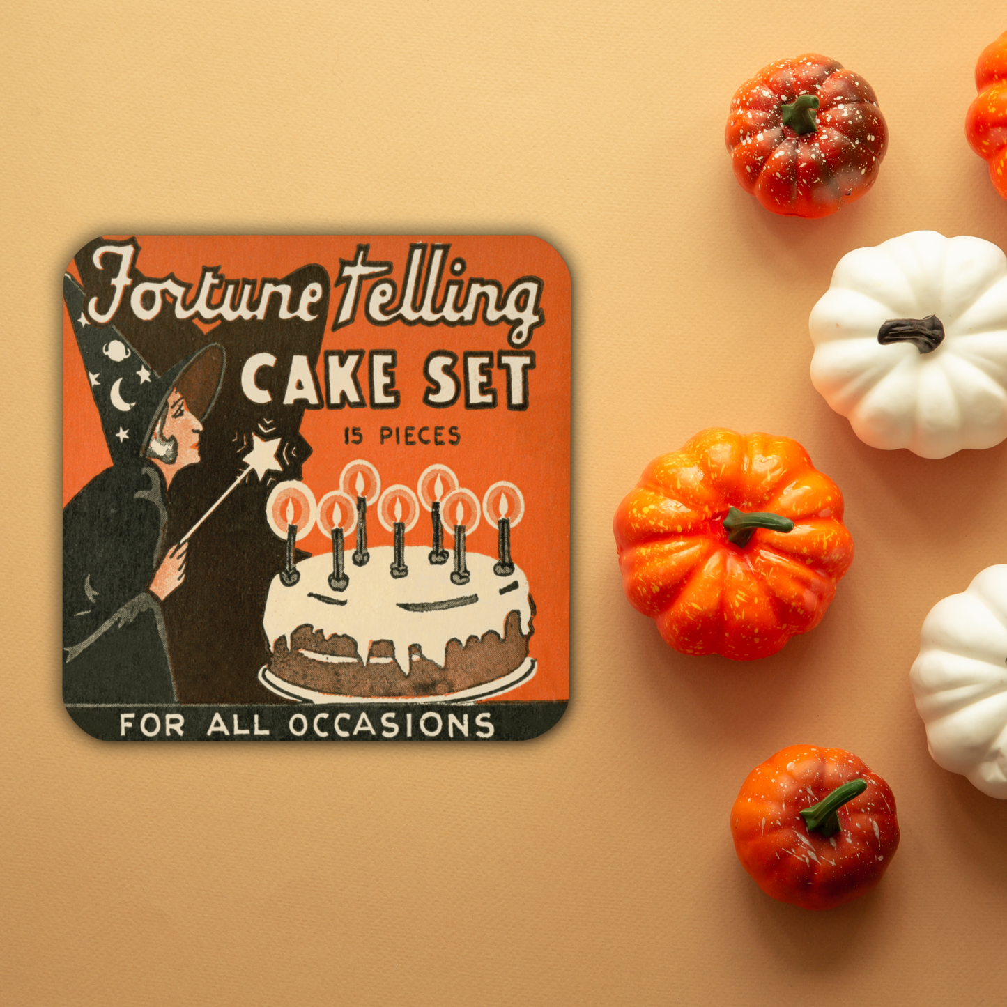 This square cork-back coaster features a retro Halloween illustration that says Fortune Telling Cake Set 15 pieces. There is a witchholding a star magic wand that she is waving over her cake with candles.