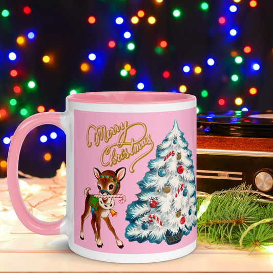 This pink lined ceramic glossy mug features a retro Mid Century 1950s print of a reindeer with candy cane next to a white christmas tree. It features gold lettering that says Merry Christmas.